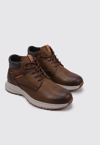 Bottines en cuir marron avec un col rembourré, des lacets contrastants, une semelle en caoutchouc et descoutures décoratives sur le côté.