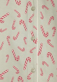 Beiger Stoff mit einem Muster aus rot-weißen, gestreiften Zuckerstangen und beigen Knöpfen entlang einer genähten Naht.