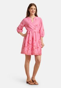 Rosenfarbenes Stoffkleid mit floralem Stickdesign, V-Ausschnitt, Dreiviertelärmeln und einem Taillengürtel. Glatte Textur und Länge über dem Knie.