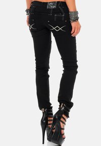 Schwarze Skinny-Jeans mit dekorativen Nähten, ausgestattet mit Gesäßtaschen mit Kreuzstichstickerei; kombiniert mit schwarzen, hochhackigen Riemchen-Stiefeln.