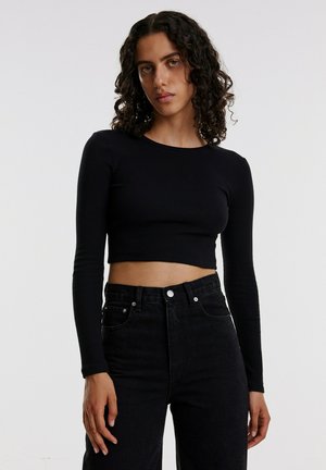 Black ribbed long-sleeve crop top paired with high-waisted black jeans. Features a round neckline and a fitted silhouette.