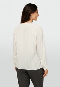 Weiße Bluse mit langen Ärmeln und vertikalen Streifen, rundem Ausschnitt und geknöpften Manschetten. Hergestellt aus leichtem Stoff, mit leicht durchscheinendem Finish.