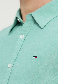 Πουκάμισο σε μέντα πράσινο με γιακά, κατασκευασμένο από υφή υφάσματος με λευκά κουμπιά. Διαθέτει μικρό κεντημένο λογότυπο σε κόκκινο, λευκό και μπλε στο στήθος.