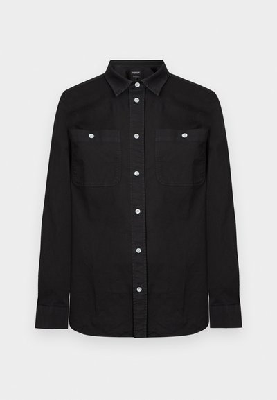 Μαύρο μακρυμάνικο πουκάμισο με κουμπιά, με μυτερό γιακά και δύο μπροστινές τσέπες στο στήθος, κάθε μία ασφαλισμένη με λευκό κουμπί.