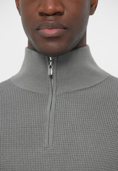 Gray, textured zip-up sweater featuring a high collar, close-fitting design, and a silver zipper detail at the neck.