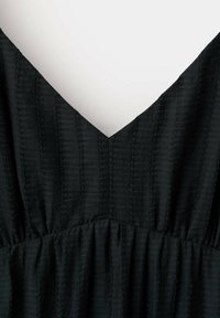 Tissu noir texturé avec un décolleté en V et une couture froncée sous la poitrine sur fond blanc.