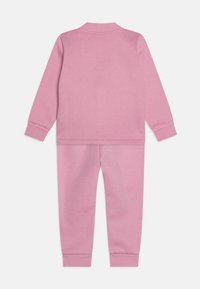 Survêtement en coton rose, comprenant un haut sans col à manches longues et un pantalon fuselé assorti. Texture lisse, poignets et taille élastiques.