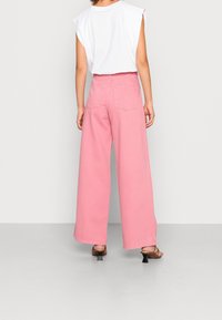 Wide-leg pink denim pants with a high waist and back pockets, paired with a loose-fitting white sleeveless top.