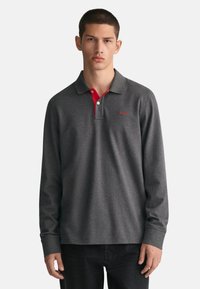 Dunkelgraues Langarm-Polohemd mit rotem Kragen und Nähten; verfügt über ein kleines Logo auf der Brust und einen klassischen Schnitt.