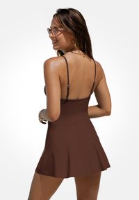 Braunes Skaterkleid mit dünnen, verstellbaren Trägern und einem schwingenden Rock. Das Material wirkt glatt und elastisch und eignet sich gut für legere Anlässe.