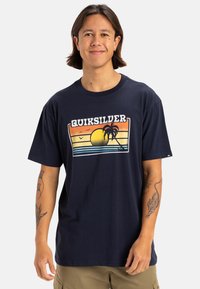 Camiseta de algodón azul marino con un estampado gráfico que incluye un sol, palmeras y rayas horizontales en naranja, amarillo y azul. Manga corta.