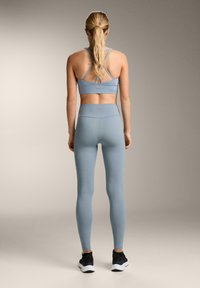 Svetlo modrý športový športový brass a legíny so hladkou textúrou, disponujúce návrhom krížového chrbta a vysokým pásom, skombinované s čiernymi teniskami.