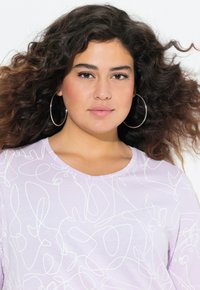Top de cuello redondo en un suave tono púrpura claro que presenta un patrón de dibujos lineales blancos fluidos. Textura suave con un corte relajado y mangas cortas.