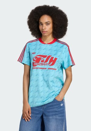Lyseblå t-shirt med et subtilt mønster, rød halsudskæring og røde stribede ærmer. Har iøjnefaldende rød tekst "Fly Tanzbar" på forsiden.