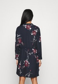 Blumenkleid aus marineblauem Stoff mit langen Ärmeln, taillierter Taille und großen burgunderfarbenen Blumenmustern. Glatte Textur und klassisches Kragendesign.
