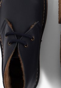 Granatowe skórzane buty z okrągłym noskiem, z miękkim brązowym futerkiem w środku i plecionymi sznurówkami. Ozdobione kontrastującym przeszyciem i metalowymi oczkami.