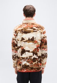 Μπουφάν από φλις σε μπεζ χρώμα με καφέ και πορτοκαλί αφηρημένα σχέδια. Διαθέτει ψηλό γιακά και ελαστικές μανσέτες. Λείο υφή.