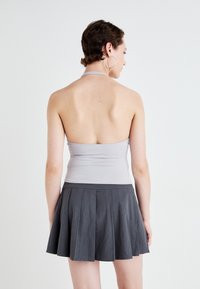 Šedý halter top s přiléhavým tělem, spárovaný s tmavě šedou plisovanou mini sukní. Hladká textura s čistým designem, bez viditelných vzorů.