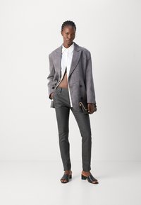 Grauer übergroßer Blazer, weißes Button-Up-Hemd, graue schmal geschnittene Hose, schwarze Schlippersandalen und eine kleine schwarze Handtasche mit Kettendetails.