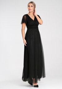 Schwarzes bodenlanges Kleid aus leichtem Stoff mit durchsichtigen, ausladenden Ärmeln und einem Wickeloberteil. Glatte Textur und elegante Silhouette.