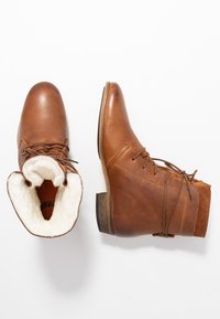 Bottines en cuir marron avec un design à lacets, doublure douce en crème, talon empilé et un mélange de textures lisses et en daim.