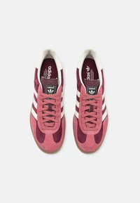 Zapatillas Adidas con parte superior de ante en rosa y burdeos, acentos en franjas blancas y suela de goma. Cuenta con cierre de cordones y lengüeta texturizada.