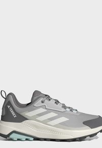 Γκρι και άσπρο παπούτσι τρεξίματος Adidas Terrex με κορδόνια και ανθεκτική σόλα για εξωτερική χρήση.