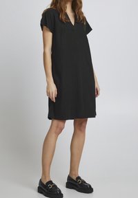 Abito in lino nero con scollatura a V, maniche corte e vestibilità rilassata. Presenta un design semplice e privo di decorazioni e arriva sopra il ginocchio.