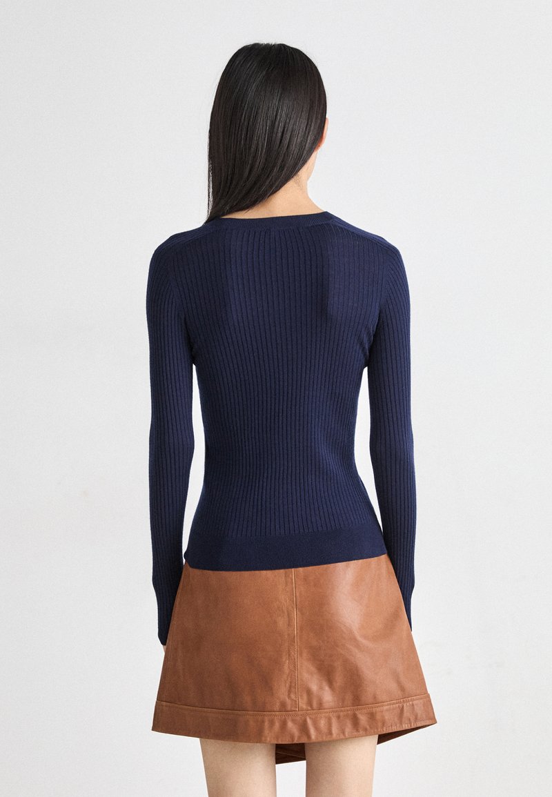 Marineblauwe geribde gebreide trui met lange mouwen, aansluitend ontwerp en een ronde halslijn, gecombineerd met een minirok van bruin leer.