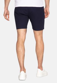 Pantaloni corti blu navy in cotone con taglio dritto, dotati di tasche laterali, una tasca posteriore e orlo pulito, abbinati a sneakers bianche.