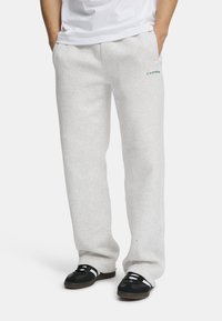 Lys grå joggebukser laget av myk stoff, med sidelommer og en liten grønn logo på forsiden. Løs passform med rette ben.