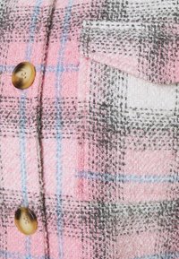 Vävd flanelltyg i rosa, vitt och grått med rutigt mönster. Har en framficka och en stor brun knapp. Känsla med textur.