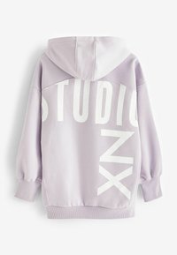 Sudadera oversize de lavanda con un estampado gráfico blanco que dice "STUDIO" y "NX" en la parte posterior; presenta una capucha con cordón y puños acanalados.