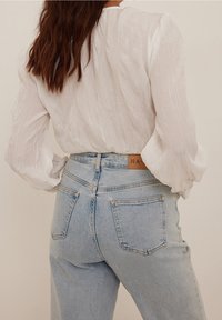 Weiße, strukturierte Bluse mit Puffärmeln, kombiniert mit hellblauen, hochtaillierten Jeans, die ein braunes Lederetikett und zwei Gesäßtaschen haben.