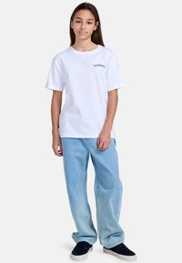 Witte katoenen T-shirt met een ronde halslijn en korte mouwen, met een zwart tekstlogo. Gecombineerd met lichtblauwe wijde jeans en donkere sneakers.