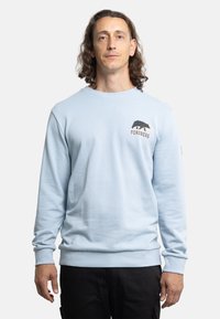 Sudadera azul claro hecha de tela suave, con cuello redondo, mangas largas y un gráfico de un oso negro con el texto "FORSBERG" en el pecho.