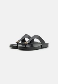Chanclas negras con suela plana, que presentan una tira central y un acento de logo dorado en el lateral. Material de plástico suave.