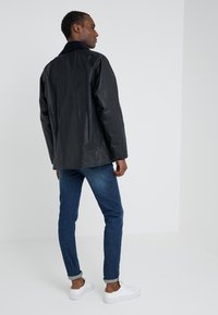 Zwarte waterdichte jas met een corduroy kraag, gecombineerd met strakke blauwe jeans en witte sneakers. Glad textuur, klassiek ontwerp en knoopdetails.
