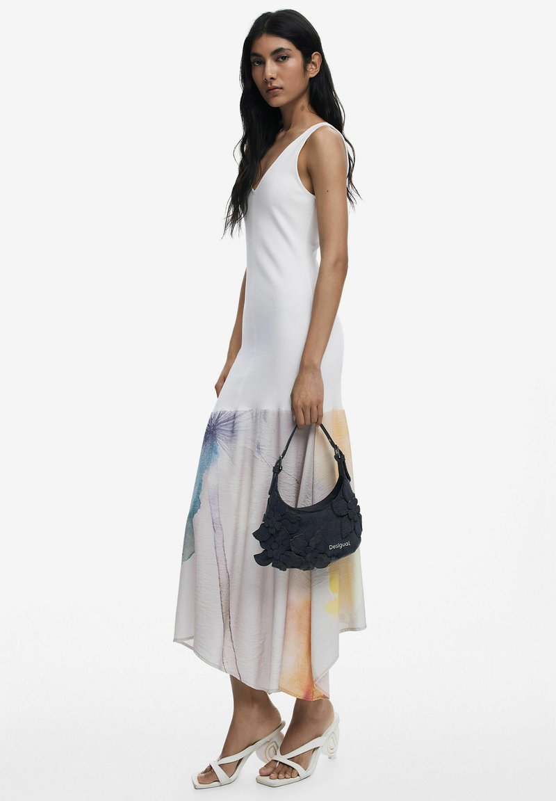 White sleeveless dress with a color gradient at the hem, paired with a textured navy handbag featuring floral accents and open-toe white heels.