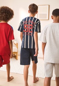 Groupe de trois enfants de dos, vêtus de vêtements décontractés : chemise rouge et short, chemise rayée marine, chemise grise et short.