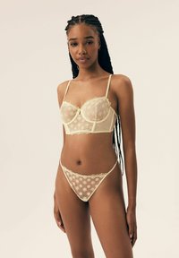 Koronkowy zestaw bielizny w jasnym żółtym kolorze, z kwiatowym haftem, z biustonoszem na drutach z regulowanymi ramiączkami oraz pasującym przezroczystym stringami.