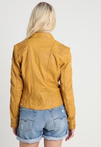 Gul läderjacka med texturerade axlar och bakpanel, med kontrasterande sömmar och en figursydd design. Kort längd.