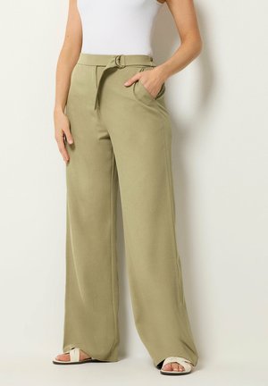 Kvinde iført vidtbenede, højtaljede bukser i lys olivengrøn med bælte og lommer, kombineret med hvid ærmeløs top og hvide sandaler.