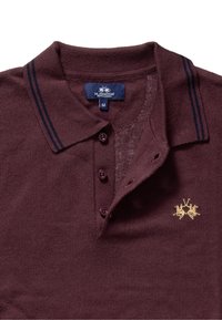 Polo burdeos con acabado texturizado, dos rayas azul oscuro en el cuello, tres botones y un logo bordado en dorado con dos caballos.