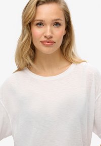 Camiseta blanca de mangas cortas en un tejido ligero y texturizado, con cuello redondo y un corte relajado.