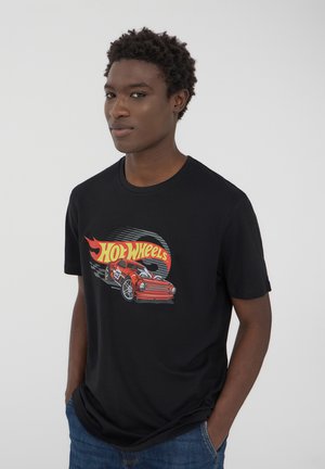 T-shirt in cotone nero con una grafica vivace di un'auto Hot Wheels rossa, decorata con fiamme e uno sfondo a scacchi. Maniche corte, design a girocollo.