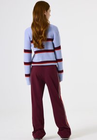 Hellblauer gerippter Pullover mit roten und dunkelblauen Streifen, kombiniert mit bordeauxfarbenen Hosen mit weißen Seitenstreifen. Lässige Passform und Textur.
