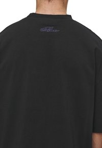 Black t-shirt made of soft cotton, featuring a relaxed fit, short sleeves, and a small purple logo embroidered at the back near the neckline.