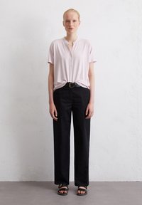 Lichtroze blouse met korte mouwen en een knoopsluiting, gecombineerd met zwarte hoge taille broek en zwarte platte sandalen. Eenvoudige, relaxte pasvorm.