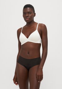 Witte naadloze bralette met dunne bandjes en een diep uitgesneden halslijn, gecombineerd met zwarte naadloze boyshorts. Glad materiaal, minimalistisch ontwerp.